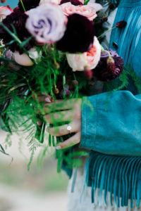 Detail shot of bouquet and engagement ring with fringe detail on jacket